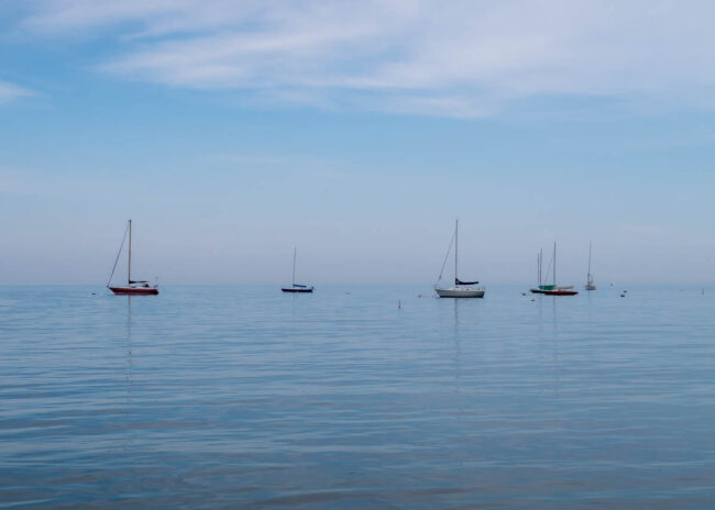 sailboats resting on very still water that is almost the same color as the sky, creating the illusion of no horizon