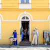A woman browses a rack of clothes outside a yellow boutique with mannequins and a display table near the entrance.