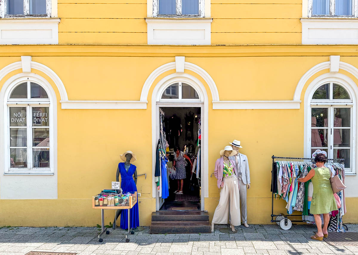 A woman browses a rack of clothes outside a yellow boutique with mannequins and a display table near the entrance.
